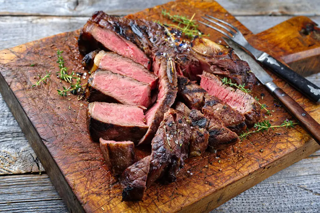Close-up of bistecca alla Fiorentina bone with charred grill marks, juicy rare meat, and rustic Tuscan presentation